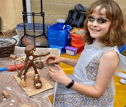 a girl wearing sunglasses making a clay model and smiling