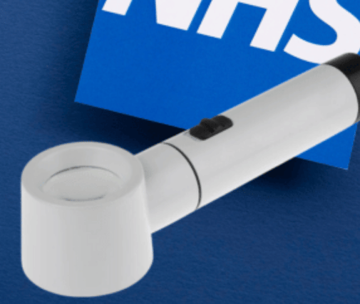 a handheld magnifier, the NHS logo can be seen in the background