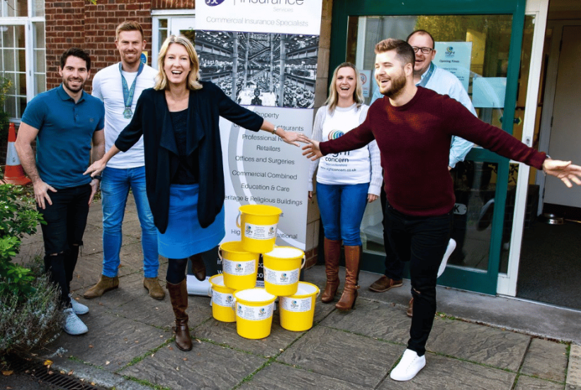A group of people smiling and some are standing on one leg, they have donation buckets next to them.
